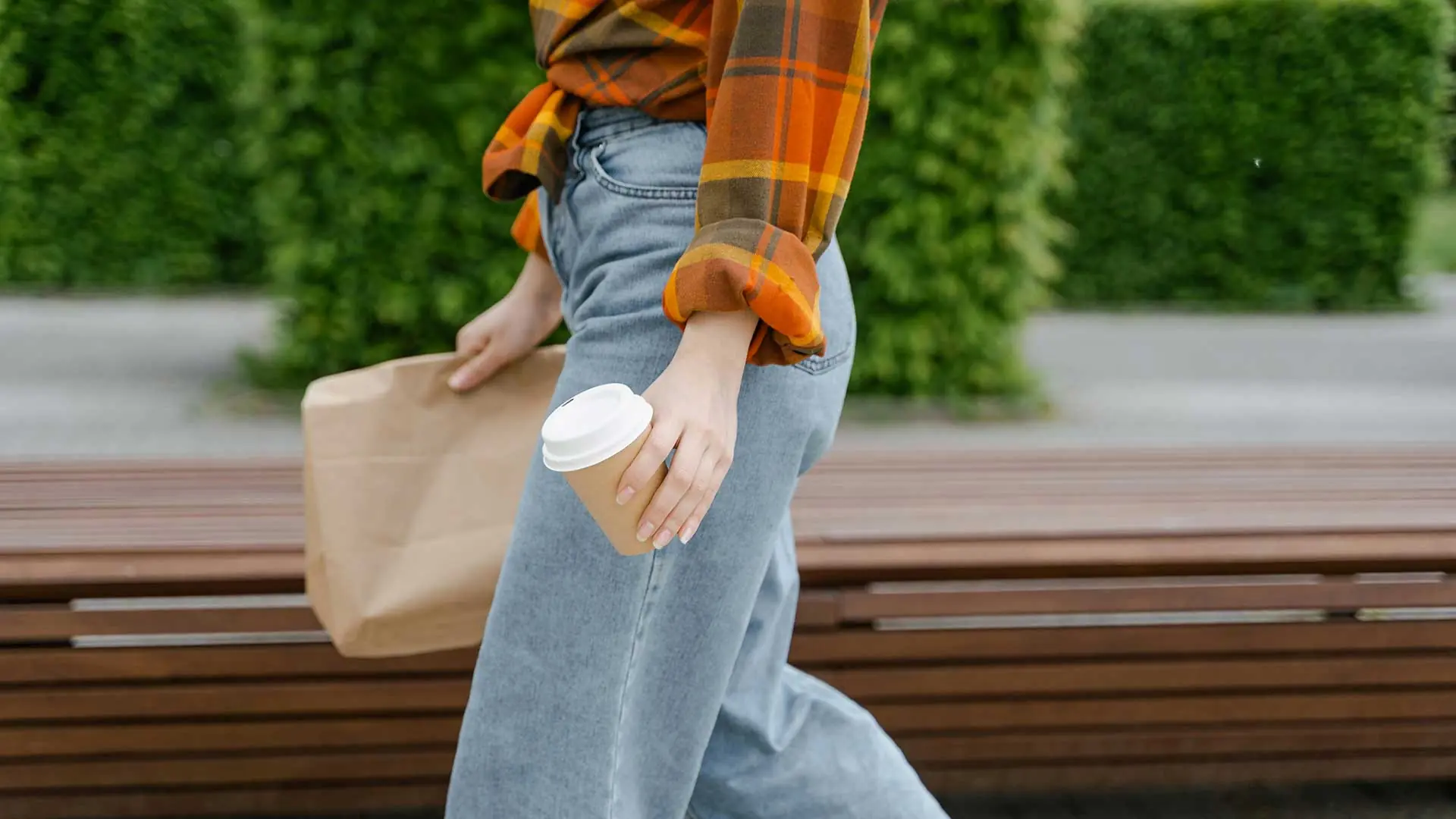 Person walking with brown paper bag and coffee cup